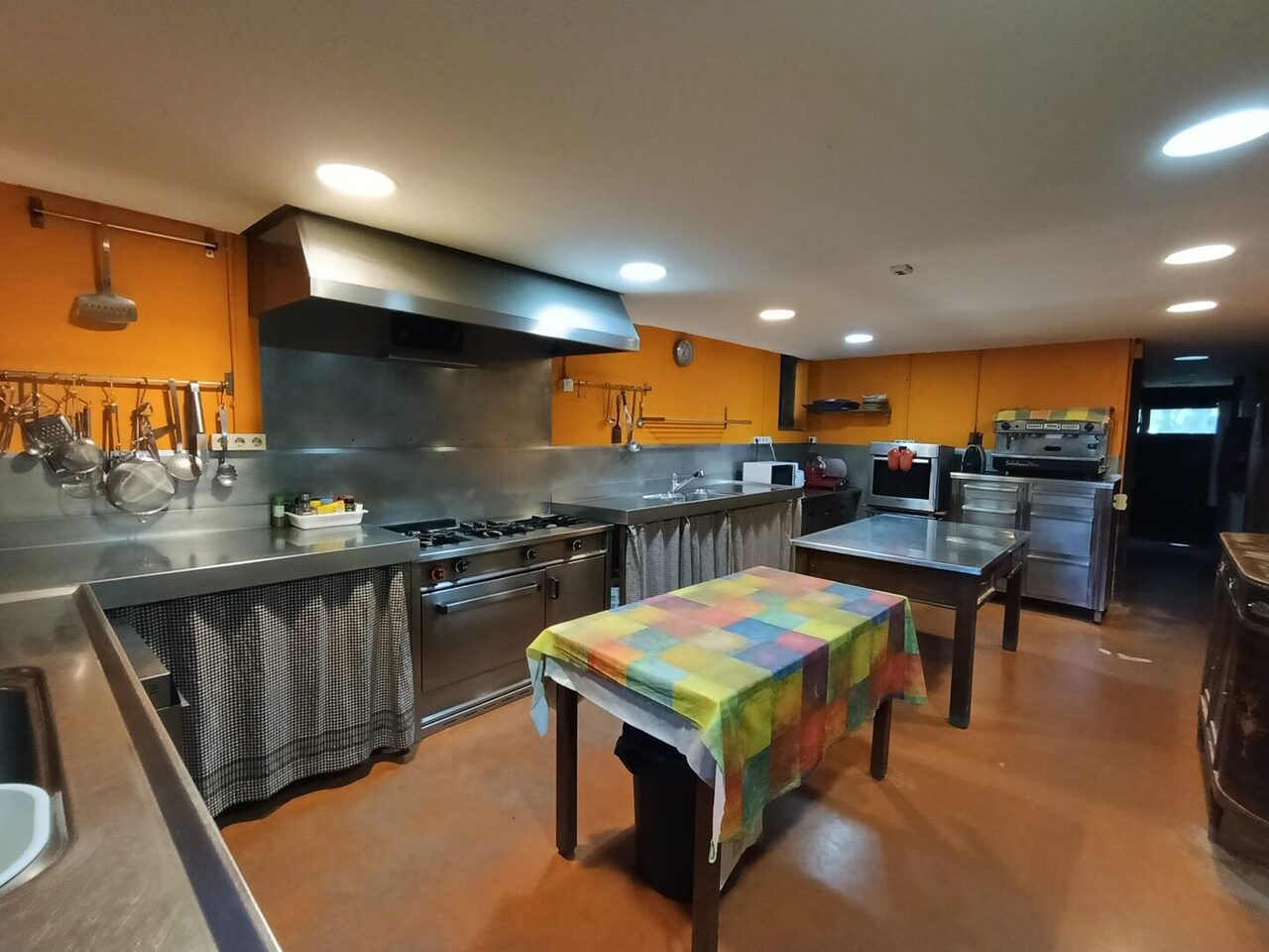 Cocina profesional de acero inoxidable con fogones, campana extractora y mesas de trabajo