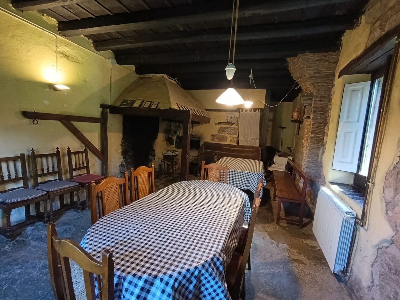 La antigua cocina del fuego en el suelo, con la campana del hogar, mesas con manteles de cuadros y bancos de madera