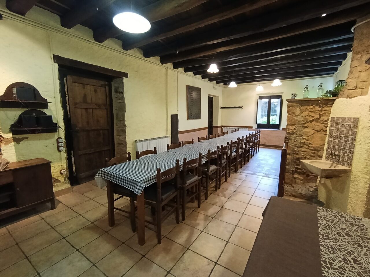 El comedor con la mesa larga puesta con manteles de cuadros, paredes de piedra y vigas de madera