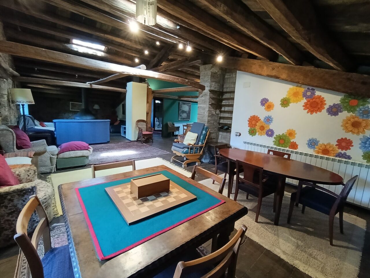 La sala de arriba, con la mesa de ajedrez, el mural de flores pintado en la pared, las butacas y las vigas vistas